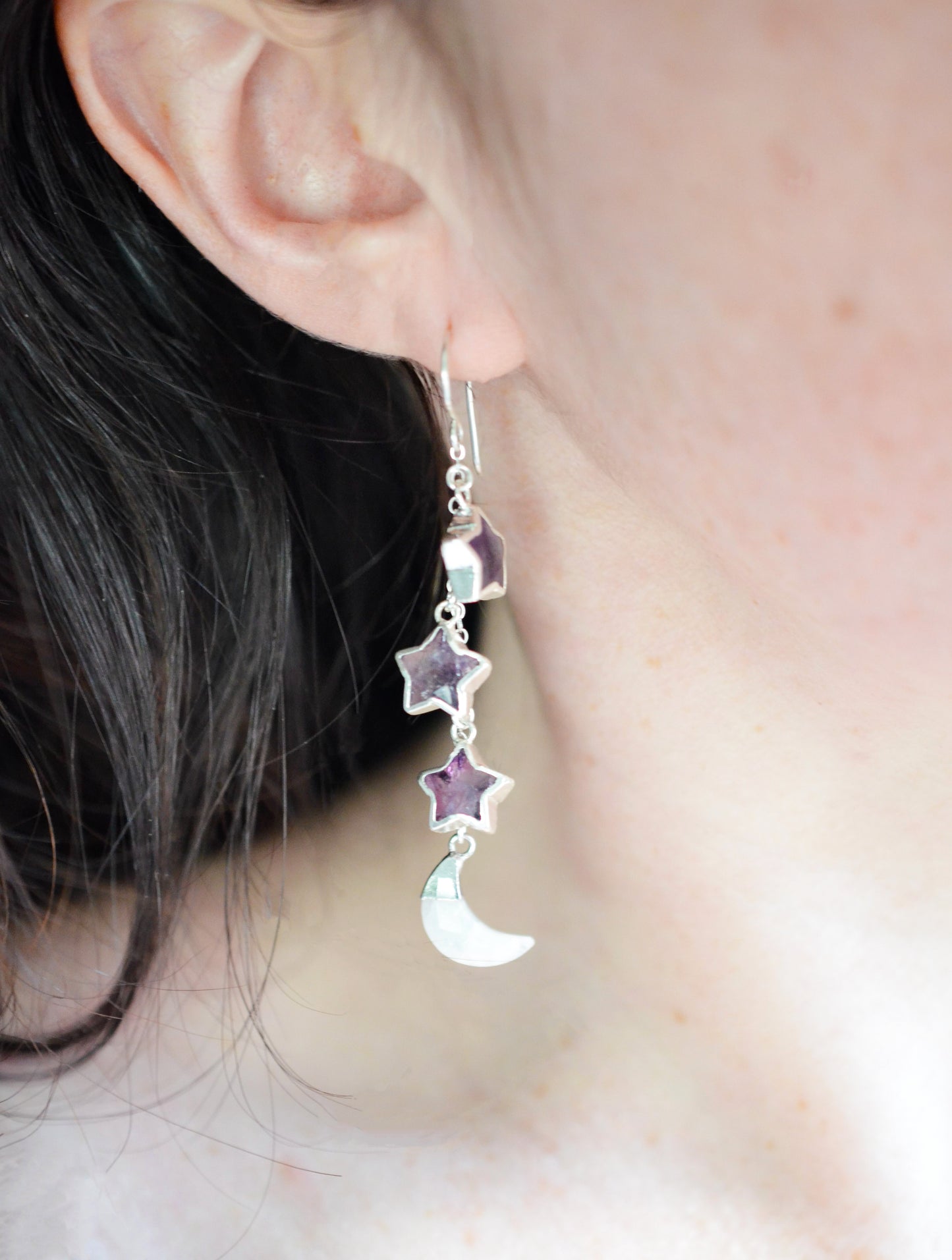 Three natural purple amethyst gemstone stars dangle atop rainbow moonstone crescent moons in these earrings. Shown in sterling silver. Modeled image.