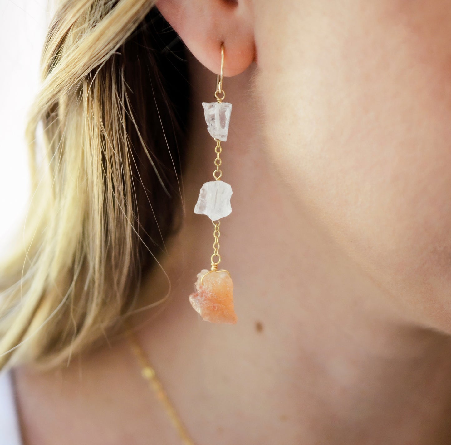 Modeled image of long clear crystal quartz and raw sunstone earring dangles.