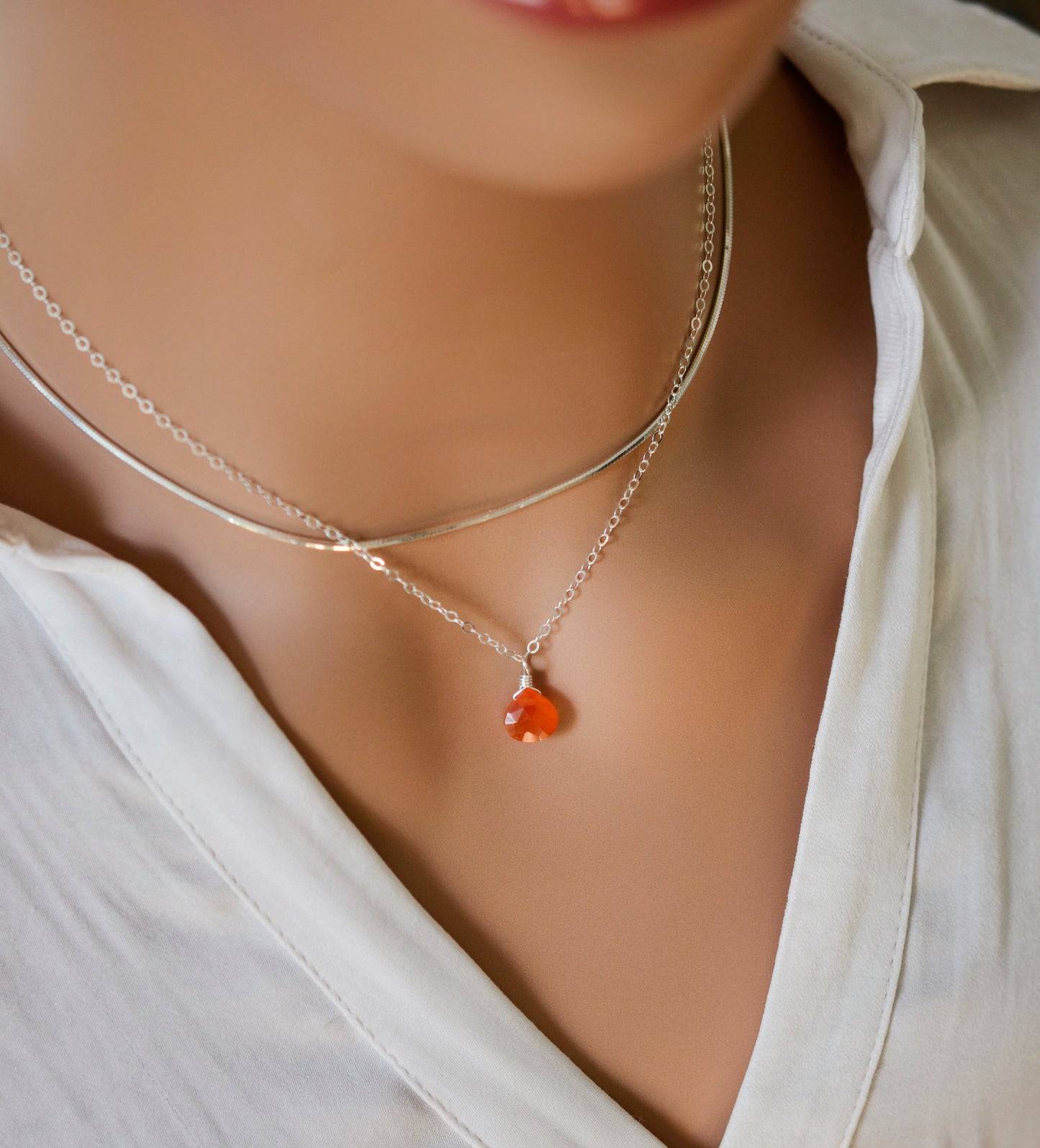 Modeled image. A small, real orange Carnelian stone teardrop pendant suspended from a sterling silver cable chain. This necklace is handmade and also comes in 14k gold filled. The crystal is faceted and varies in shades of orange to red.