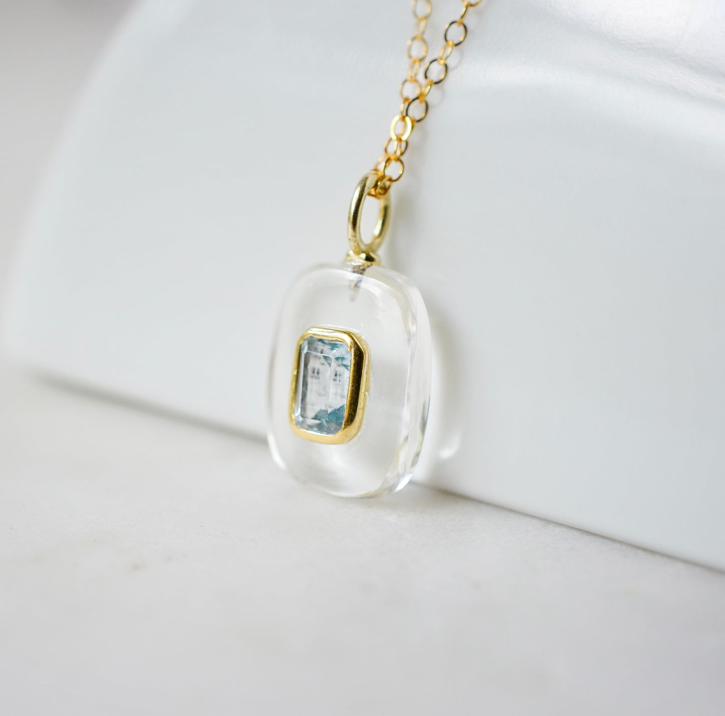 Side view. Handmade Maris necklace featuring a Blue Topaz set inside a clear Rock Crystal frame on a 14K Gold Filled chain. Ideal gift for wife, girlfriend, or mom. Minimalist topaz pendant for layering.
