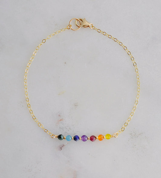 A dainty, minimalist chakra pride beaded chain bracelet handmade with small natural gemstones in rainbow colors.