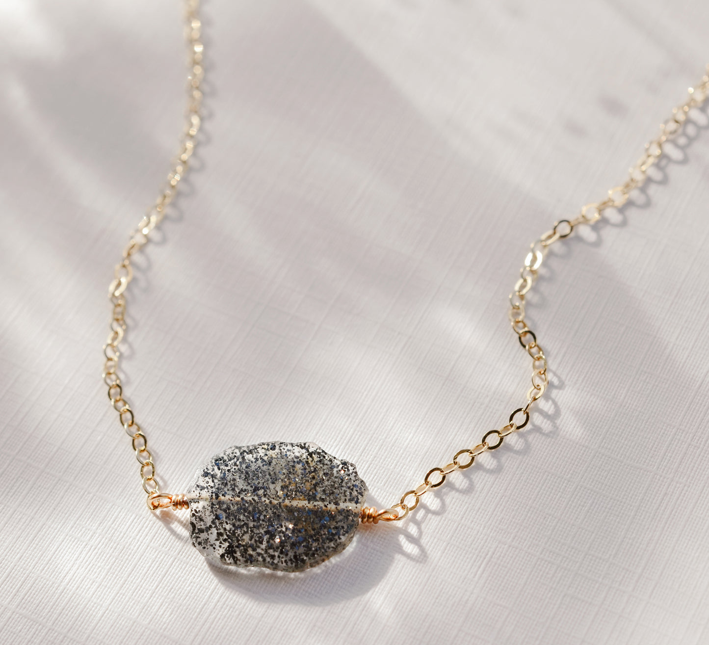 Close up image of raw slice of natural black sunstone set on a 14k gold filled chain.