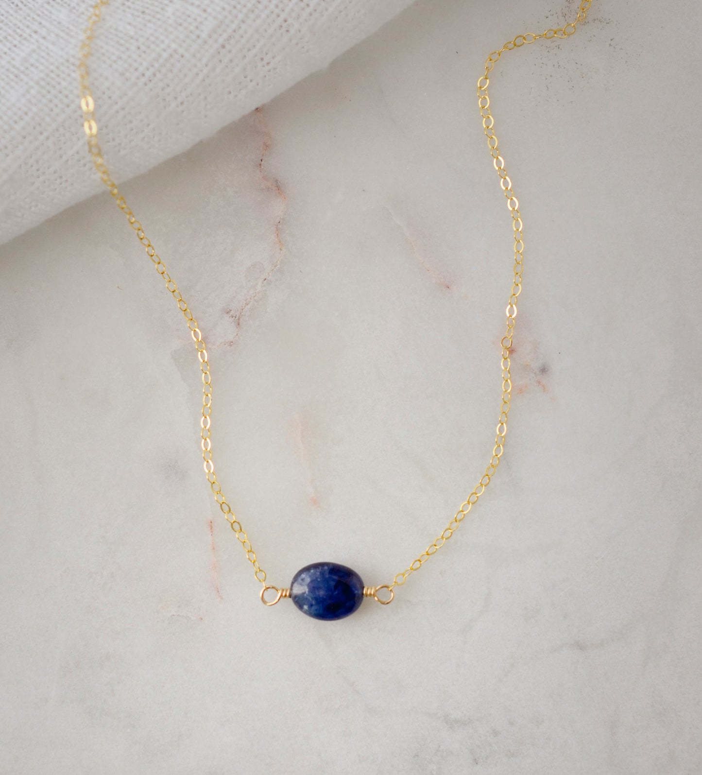 Small blue sapphire stone set onto a gold chain. The stone is a puffed oval shape.