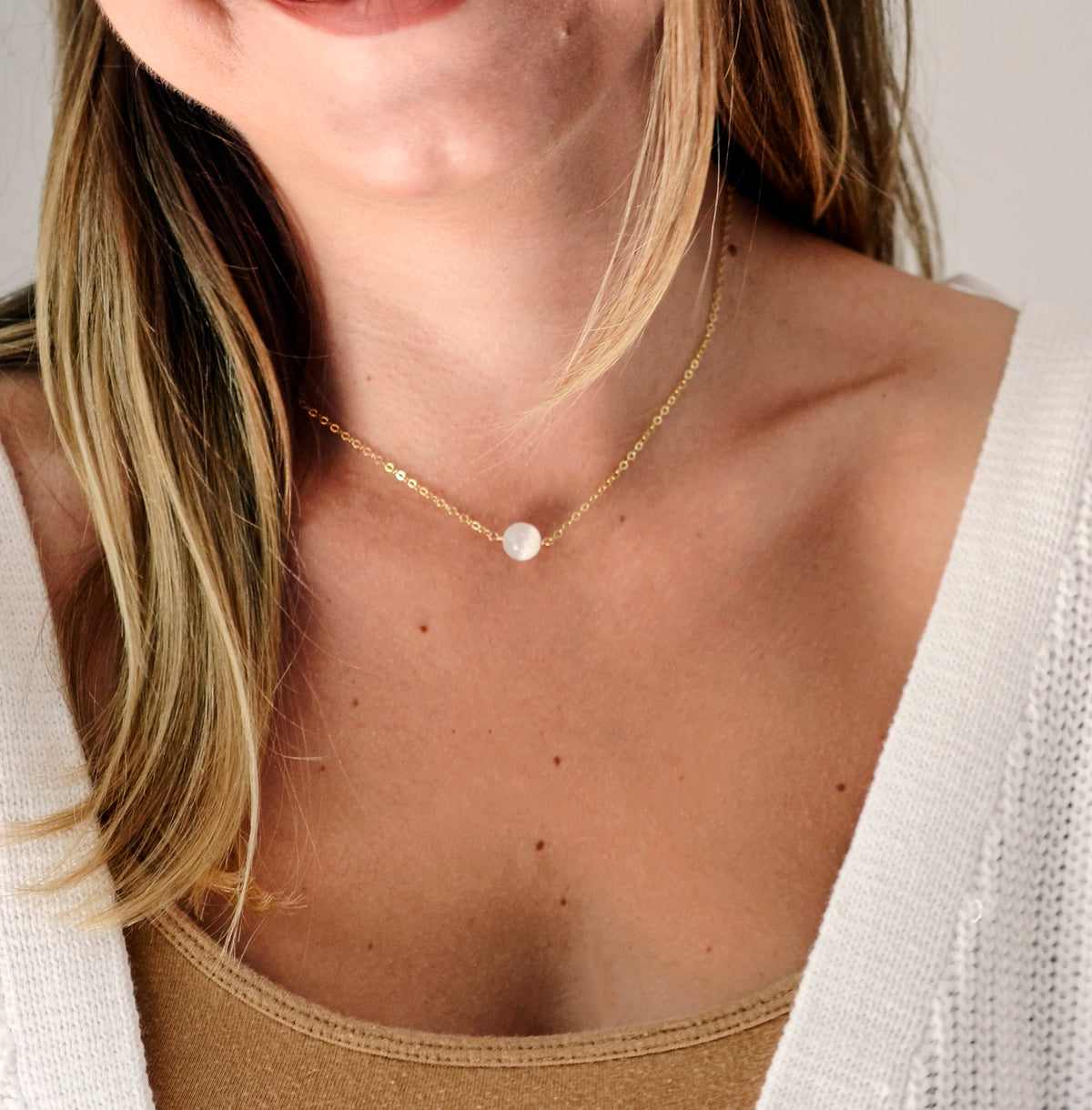 A woman wearing a small white selenite necklace with a single stone. The gemstone is smooth polished and set on your choice of a sterling silver or 14k gold filled chain.