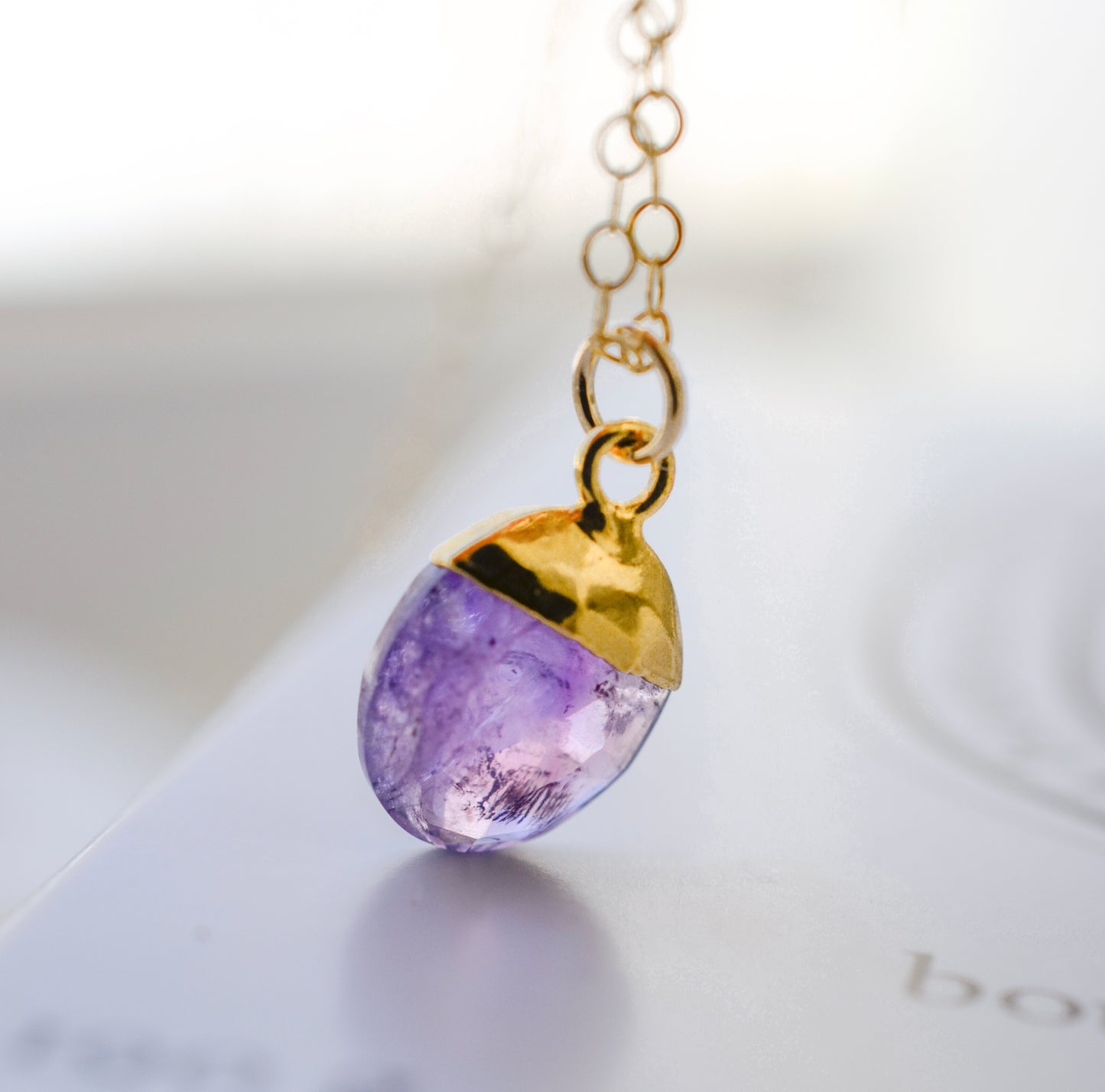 Close up of a real purple amethyst dainty stone pendant in gold. The necklace is handmade in new england by Gemnia Jewelry.