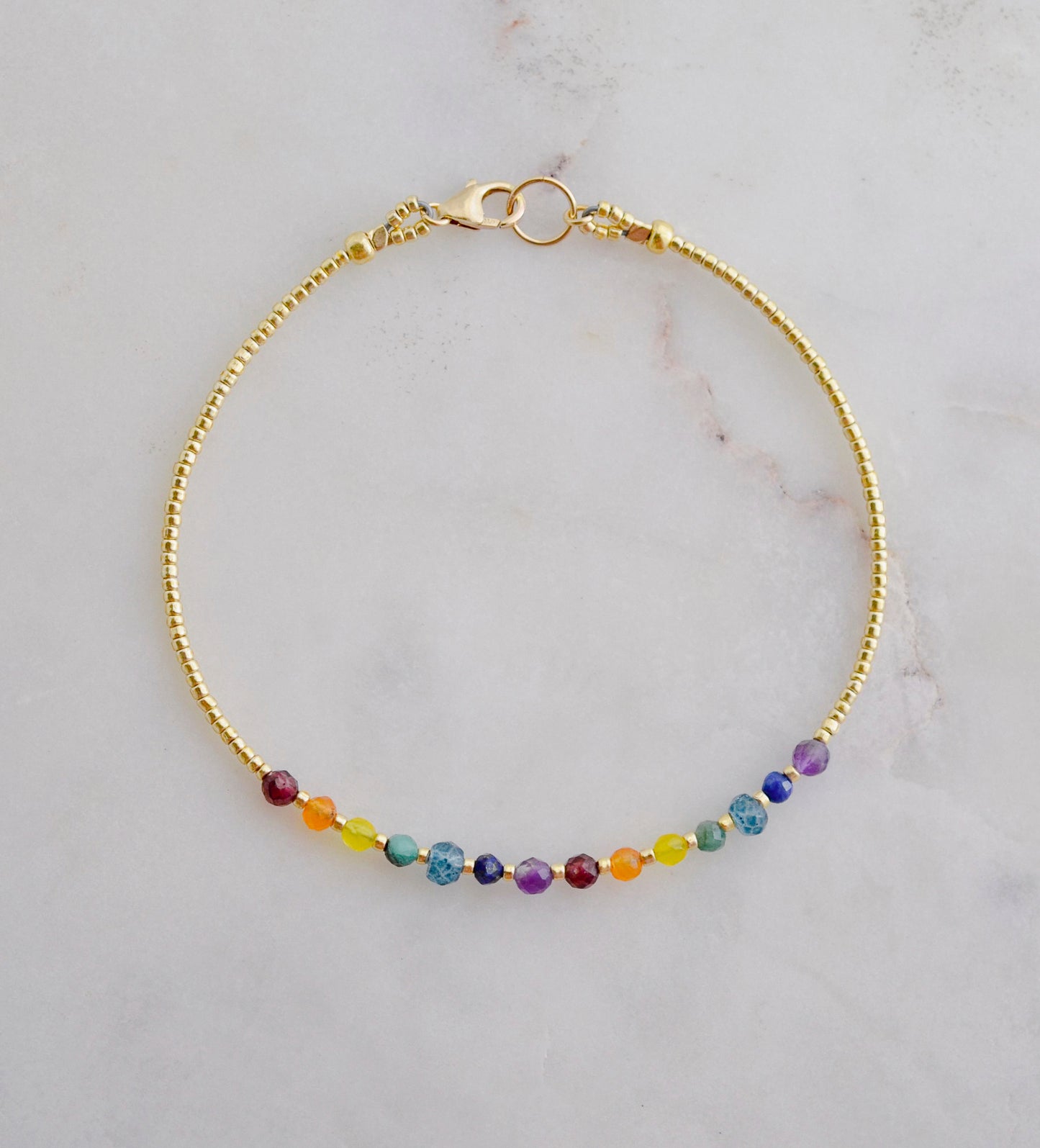 A beaded rainbow bracelet with natural crystal gemstones in the order of the chakras. This gold piece is handmade in Connecticut by Gemnia Jewelry.