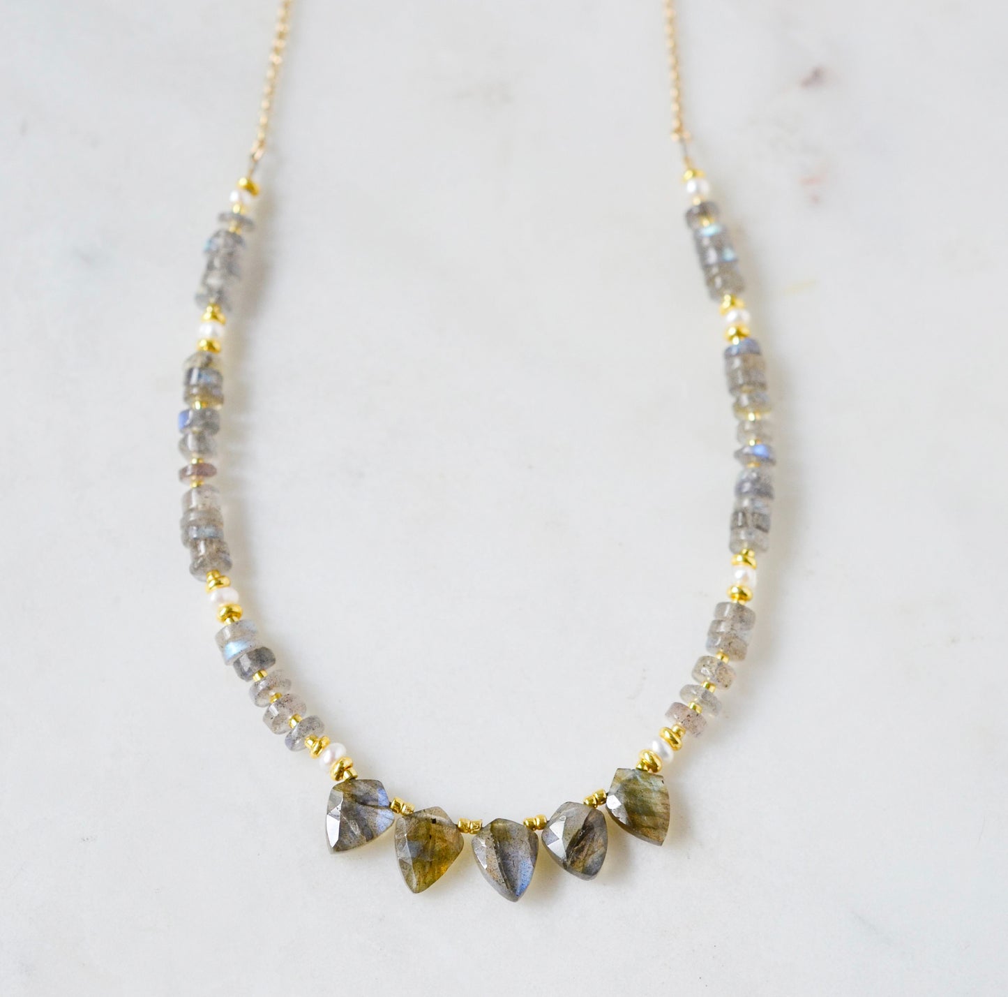 A handmade, beaded labradorite and pearl gemstone necklace with five labradorite teardrops in the front. Shown in 14k gold filled.