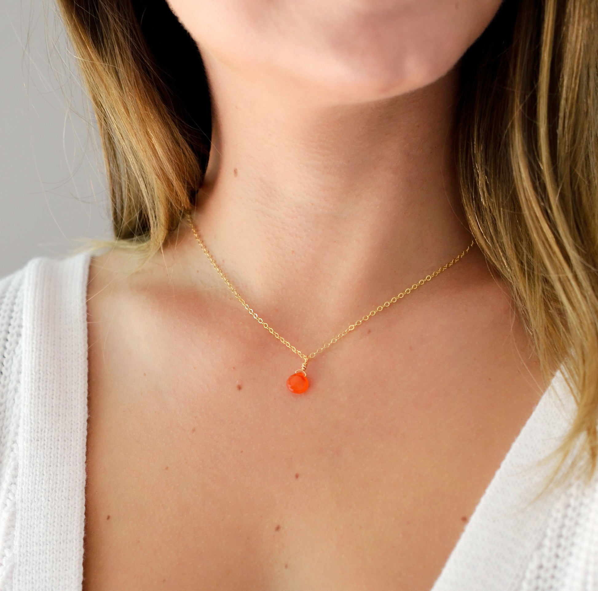 Modeled image. A delicate, genuine orange Carnelian gemstone teardrop pendant suspended from a 14k gold filled cable chain. This necklace is handmade and also comes in sterling silver.