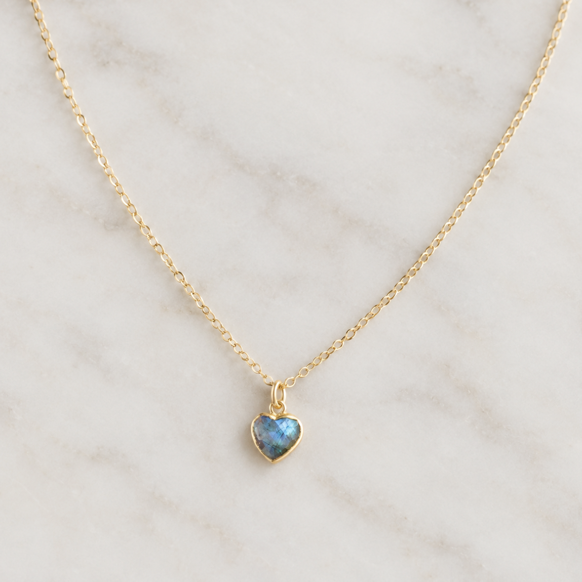 A delicate 14k gold filled chain necklace with a small heart-shaped pendant featuring a shimmering blue-gray natural labradorite gemstone. Handmade minimalist stone jewelry by Gemnia.