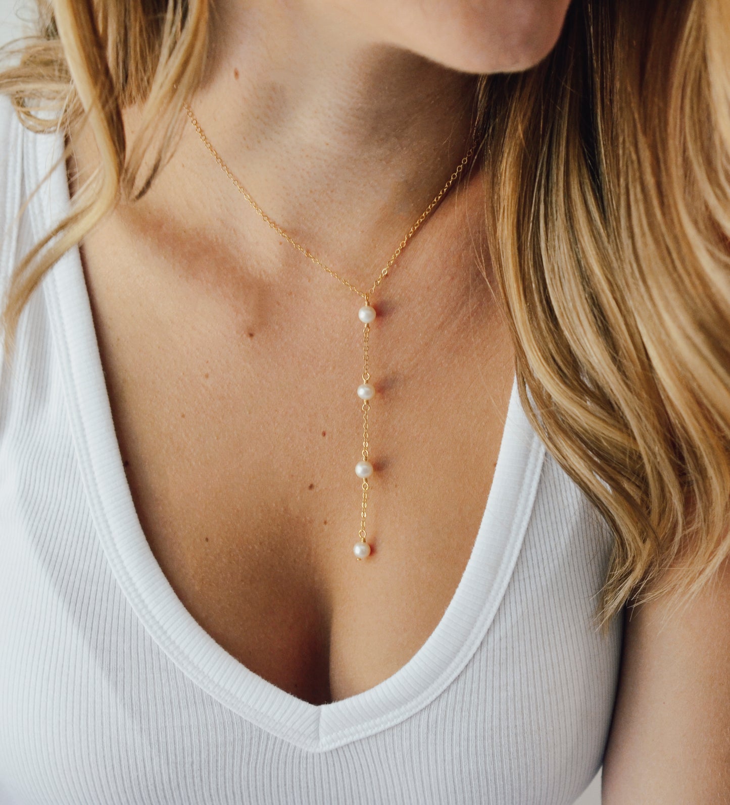 Modeled image. Four semi-round white freshwater pearls are suspended in a Y-style necklace on a 14k gold filled chain. Each pearl is approximately one inch apart. This necklace is also available in sterling silver.