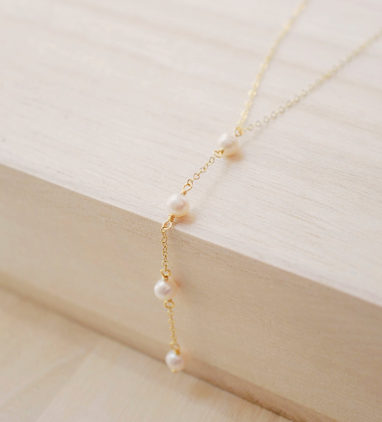 Four semi-round white freshwater pearls are suspended in a Y-style necklace on a 14k gold filled chain. Each pearl is approximately one inch apart. This necklace is also available in sterling silver.