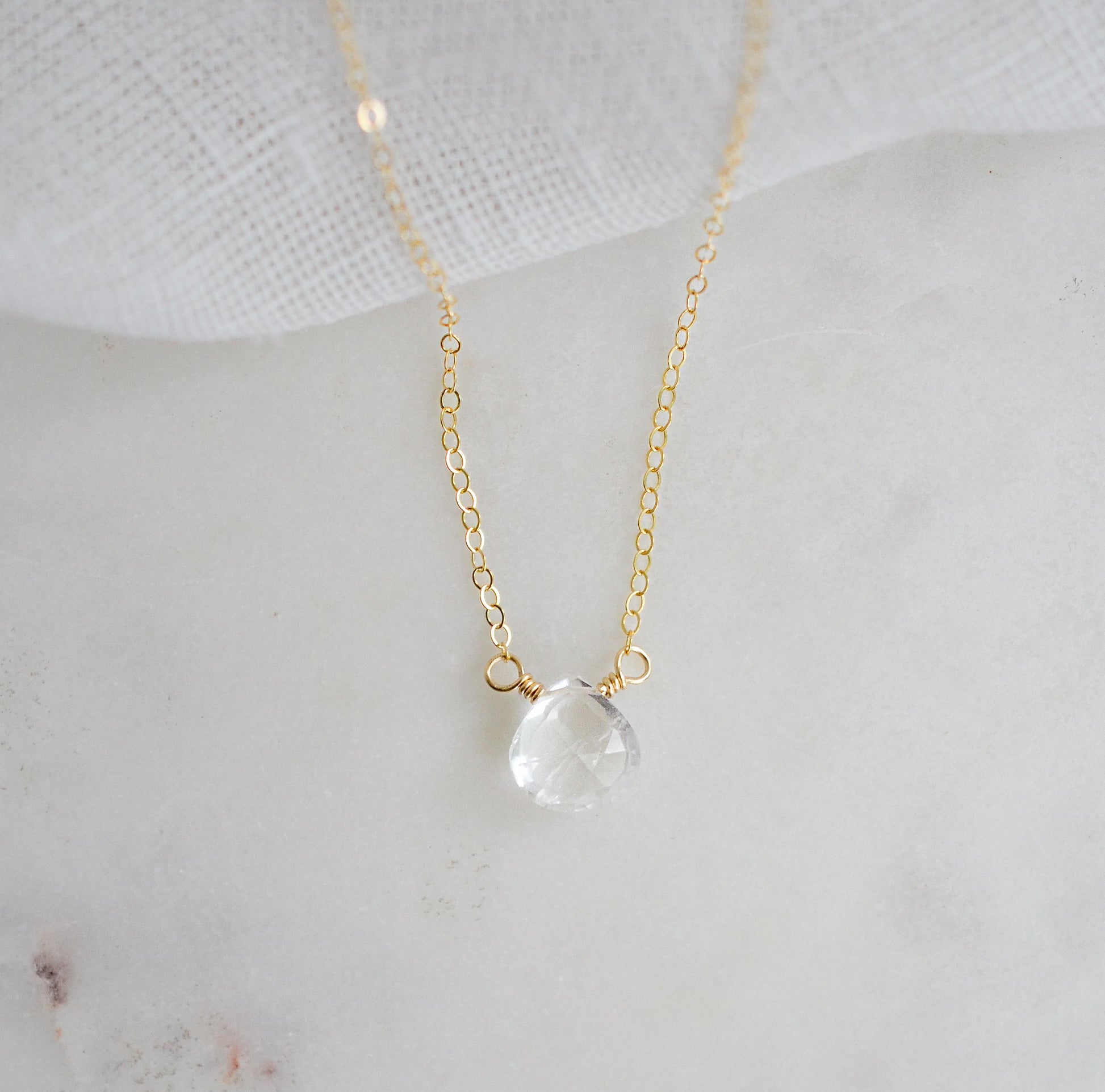 A clear, natural crystal quartz faceted teardrop set onto a 14k gold filled chain.