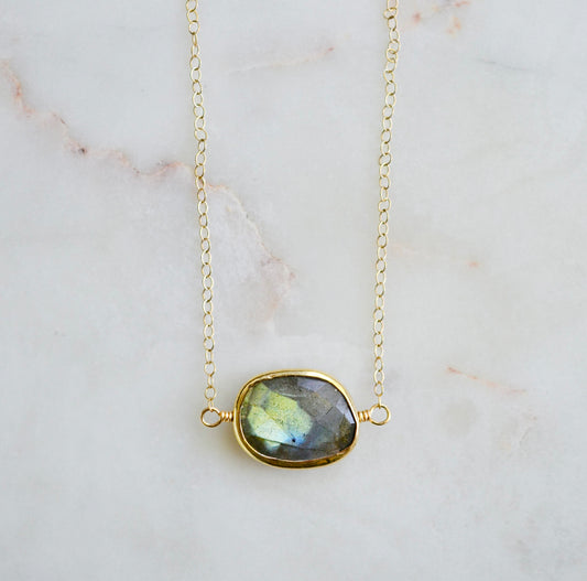A faceted, natural labradorite pendant bezeled in gold and set on a 14k gold filled chain. This necklace is also available in sterling silver. The stone is oval in shape and flashes blue, green, or yellow.