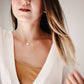 A woman wearing a natural, white, round selenite gemstone pendant on a 14k gold filled chain. The crystal/mineral is smooth polished. Handmade jewelry by Gemnia in Connecticut.