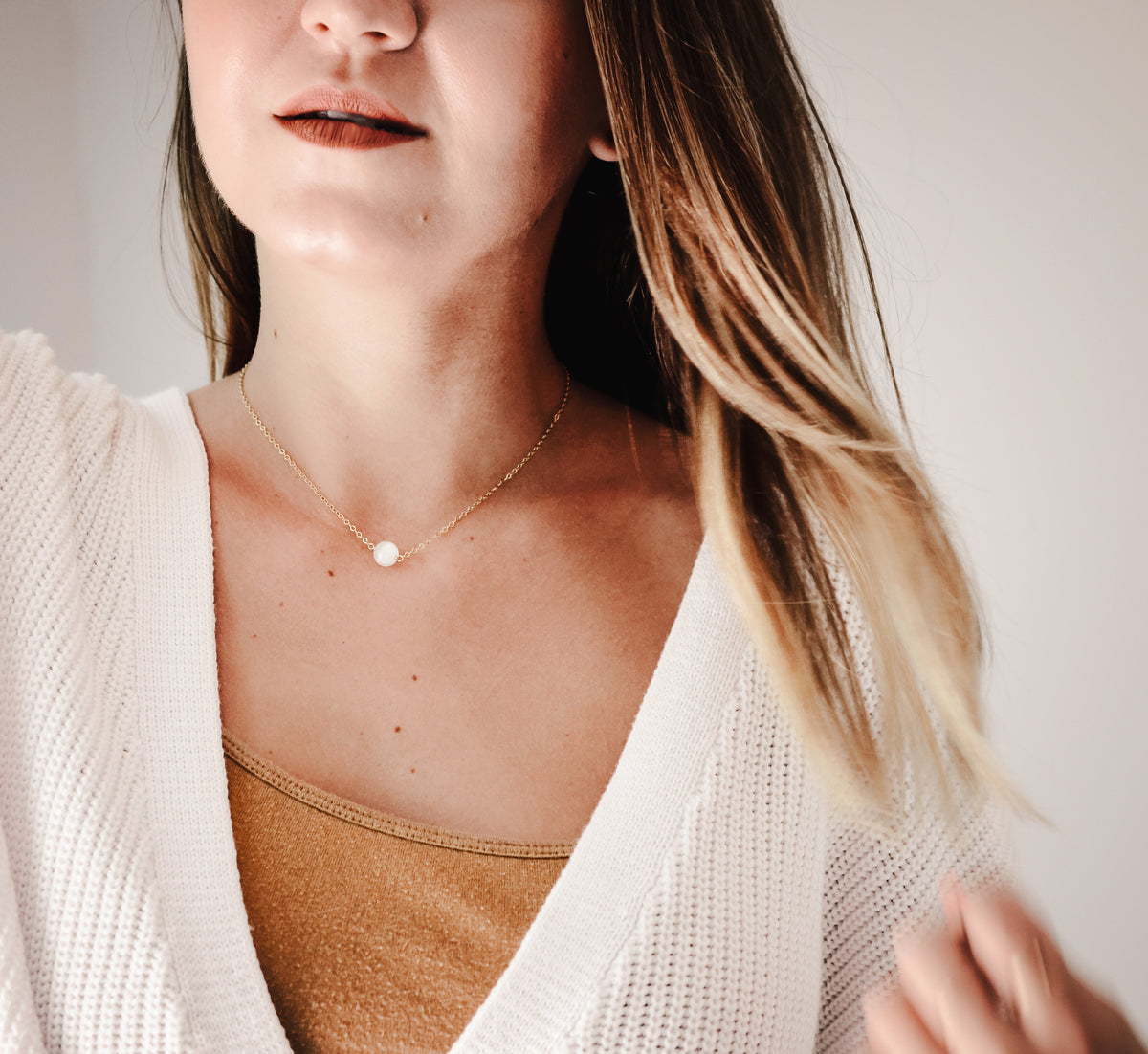 A woman wearing a natural, white, round selenite gemstone pendant on a 14k gold filled chain. The crystal/mineral is smooth polished. Handmade jewelry by Gemnia in Connecticut.