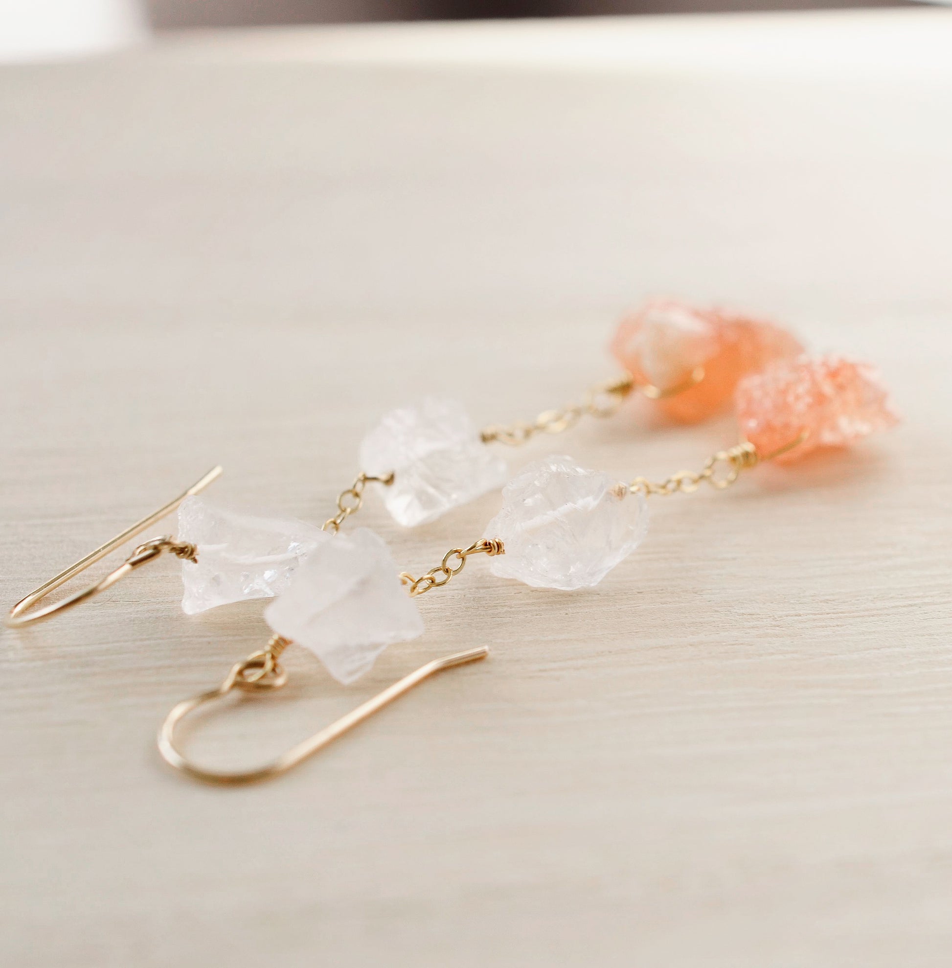 Close up image of clear crystal quartz and raw sunstone earrings in gold.