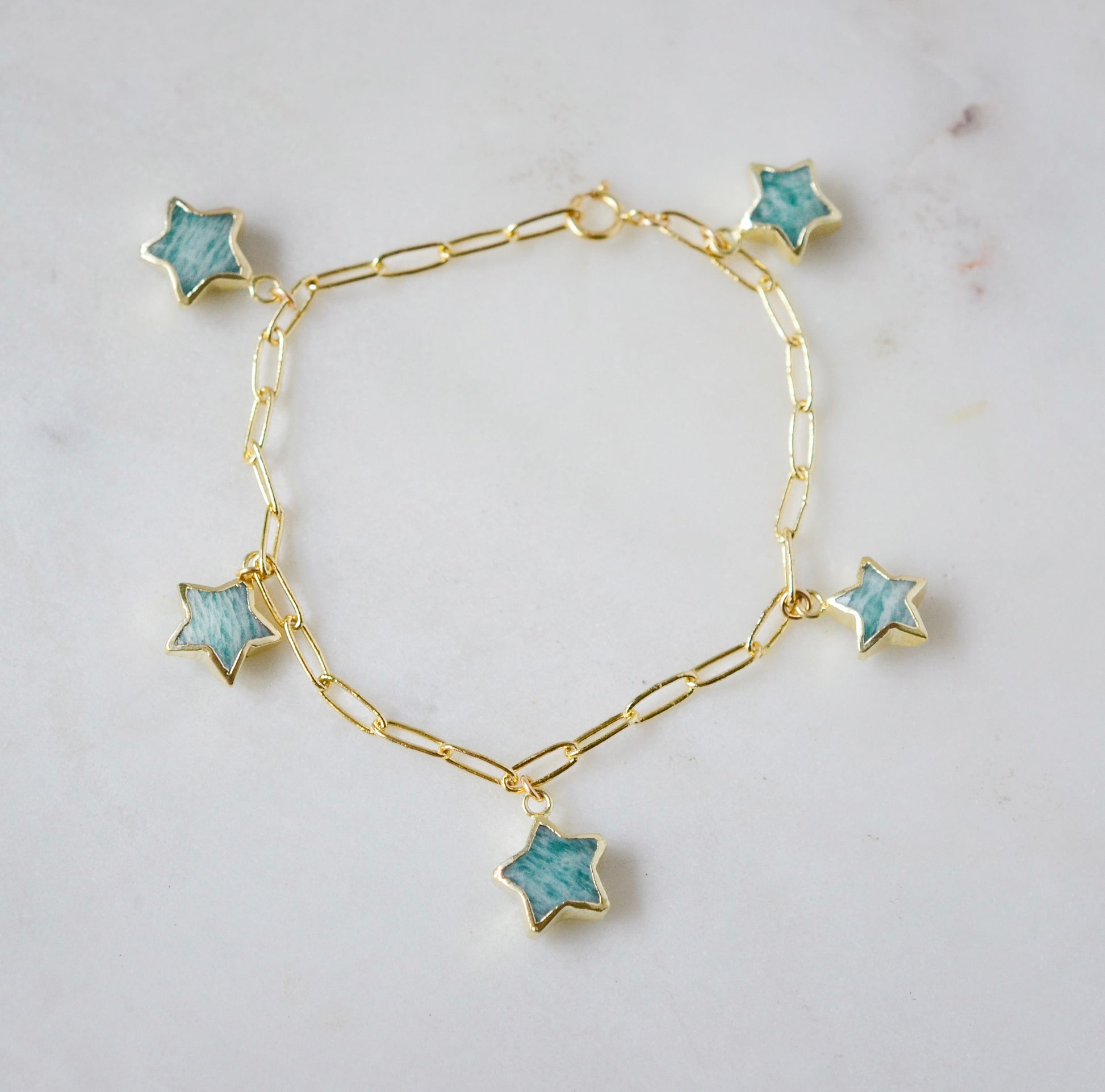 Gold bracelet with blue amazonite star-shaped gemstone charms on a light gray background.