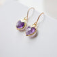 A closeup of natural purple amethyst heart dangle earrings in gold. The french earwires are 14k gold filled. Handmade in Connecticut. 