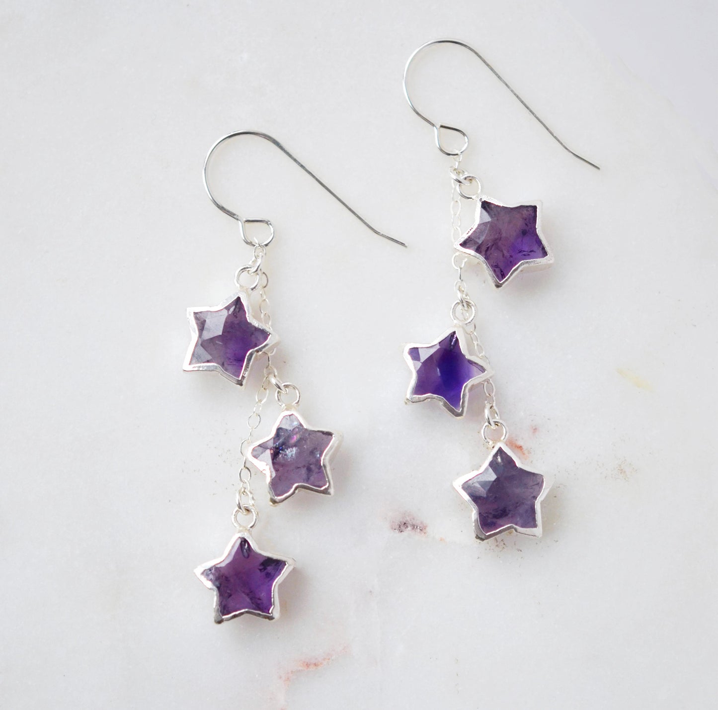 Long silver amethyst star dangle earrings. Three stars hang from a dainty chain beneath sterling silver earring hooks.