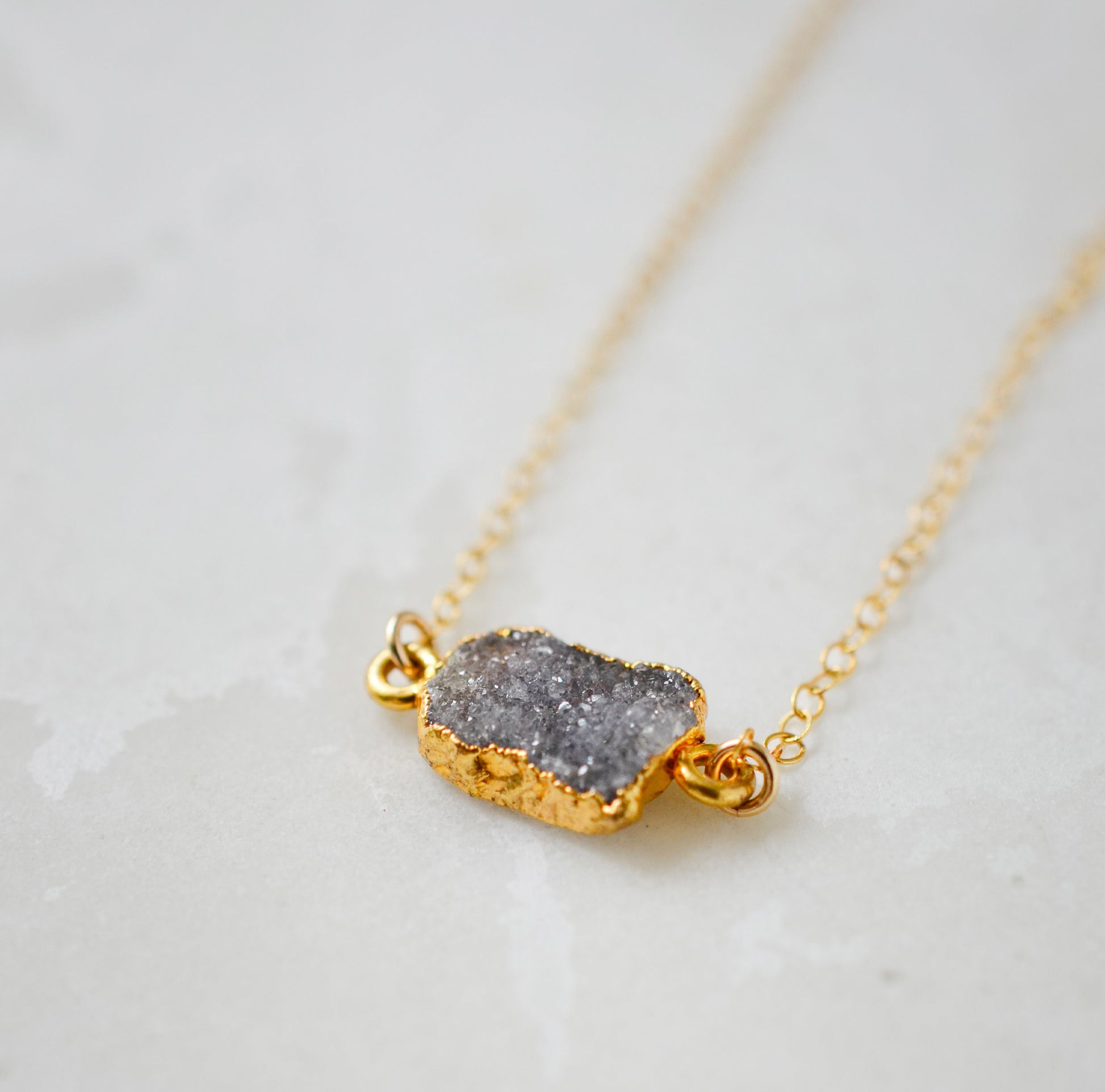 Side view of a natural black, gray druzy crystal gemstone on a 14k gold filled chain necklace.