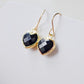 Black onyx heart earrings in gold. The stones are faceted and solid black with gold bezels surrounding their sides. The ear wires are basic hooks.
