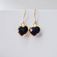 Black onyx heart earrings in gold. The stones are faceted and solid black with gold bezels surrounding their sides. The ear wires are basic hooks.