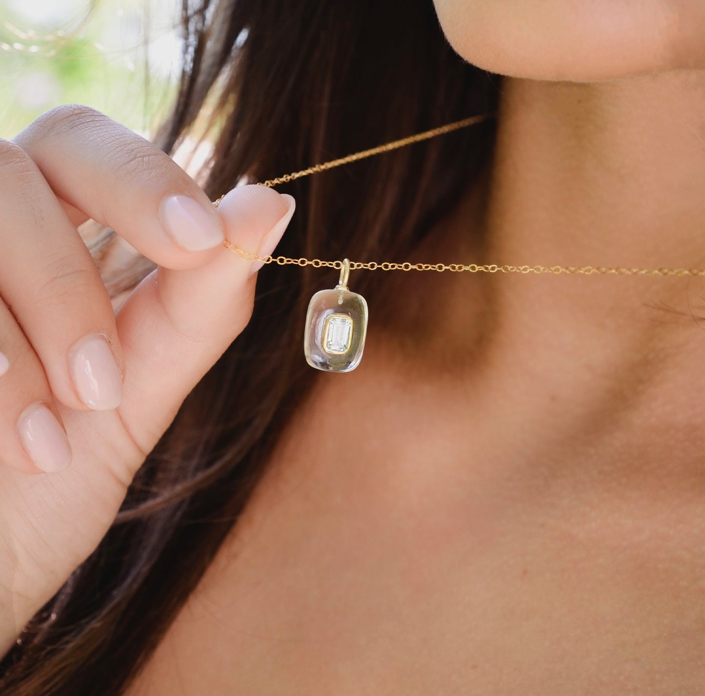 Close-up of a gold necklace with a clear pendant worn by a woman. 
Handmade Maris necklace featuring a Blue Topaz set inside a clear Rock Crystal frame on a 14K Gold Filled chain. Ideal gift for wife, girlfriend, or mom. Minimalist topaz pendant for layering.