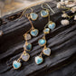 These handmade earrings feature blue and white natural stone hearts bezeled in gold. Each gemstone is a different color and includes: labradorite, larimar, mother of pearl, aquamarine, and rainbow moonstone. Long and light weight they make the perfect romantic gift. They are 3 inches long.
