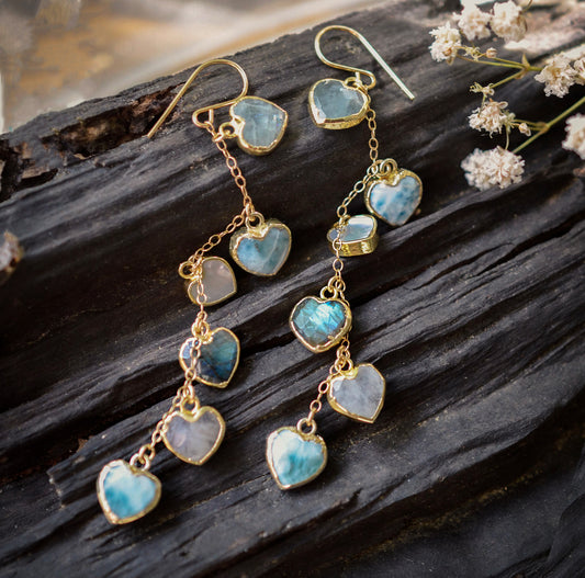 These handmade earrings feature blue and white natural stone hearts bezeled in gold. Each gemstone is a different color and includes: labradorite, larimar, mother of pearl, aquamarine, and rainbow moonstone. Long and light weight they make the perfect romantic gift. They are 3 inches long.