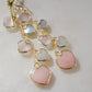 Long pink stone heart earrings in 14k gold filled. There are five heart crystal dangles hanging from a simple chain forming a cluster. The stones include: rose quartz, mother of pearl, pink opal, and rainbow moonstone. They are approximately three inches long.