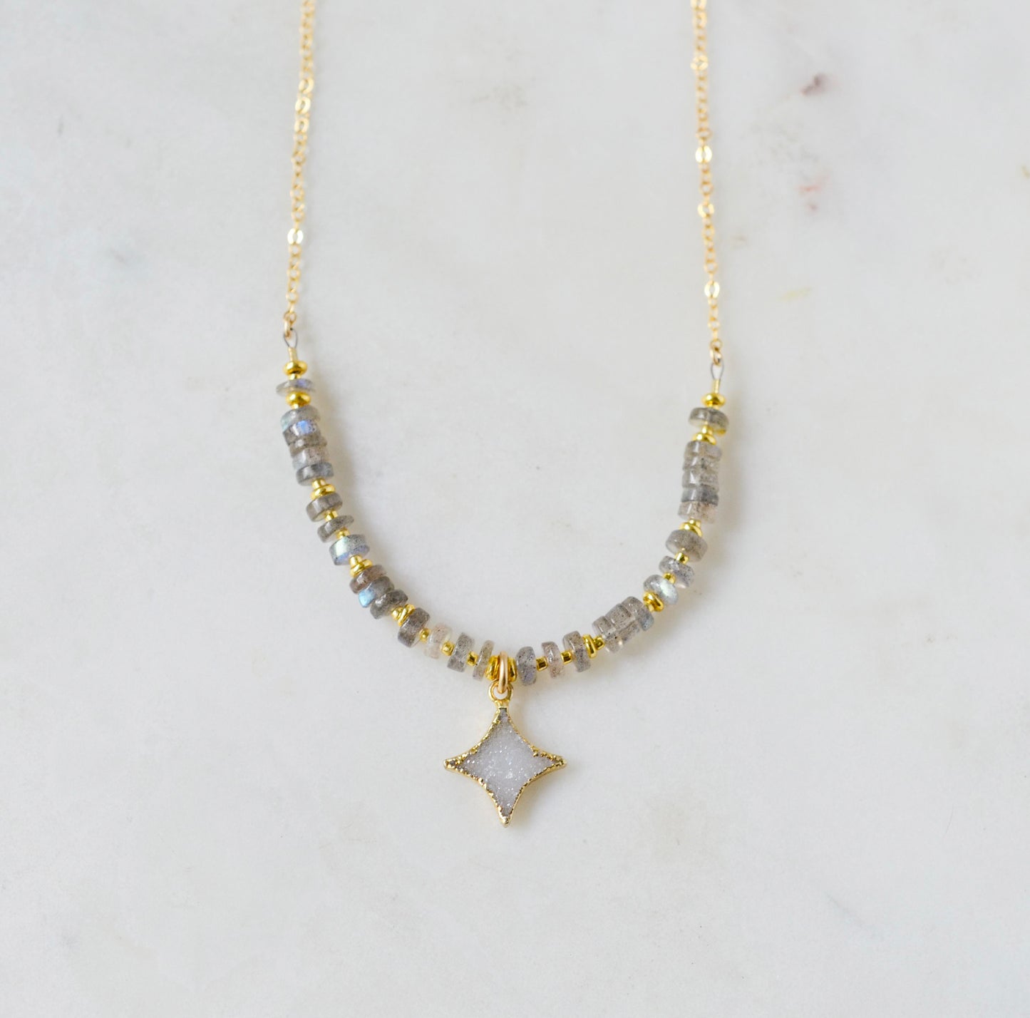 A beaded labradorite gemstone necklace with a white quartz druzy north star pendant at its center. Shown in gold.