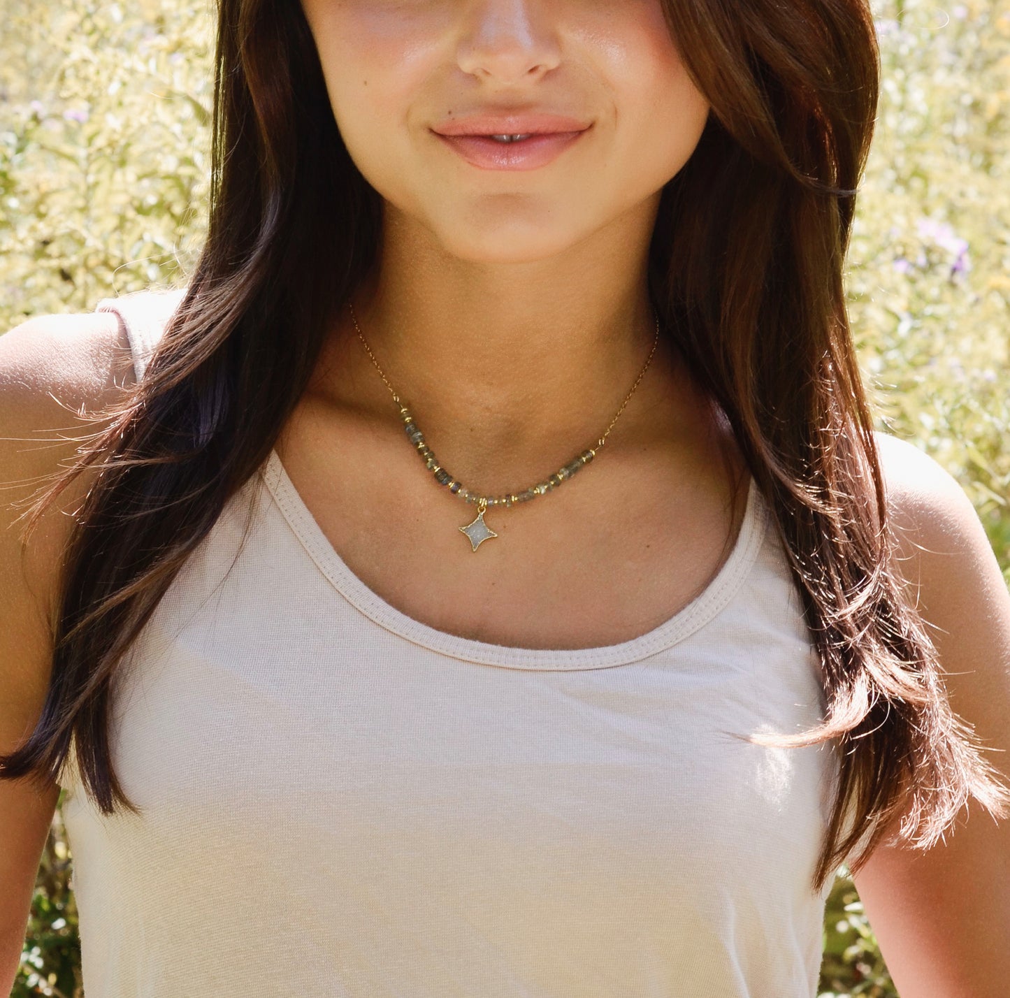 Woman wearing a beaded labradorite necklace with a star pendant in a natural setting.