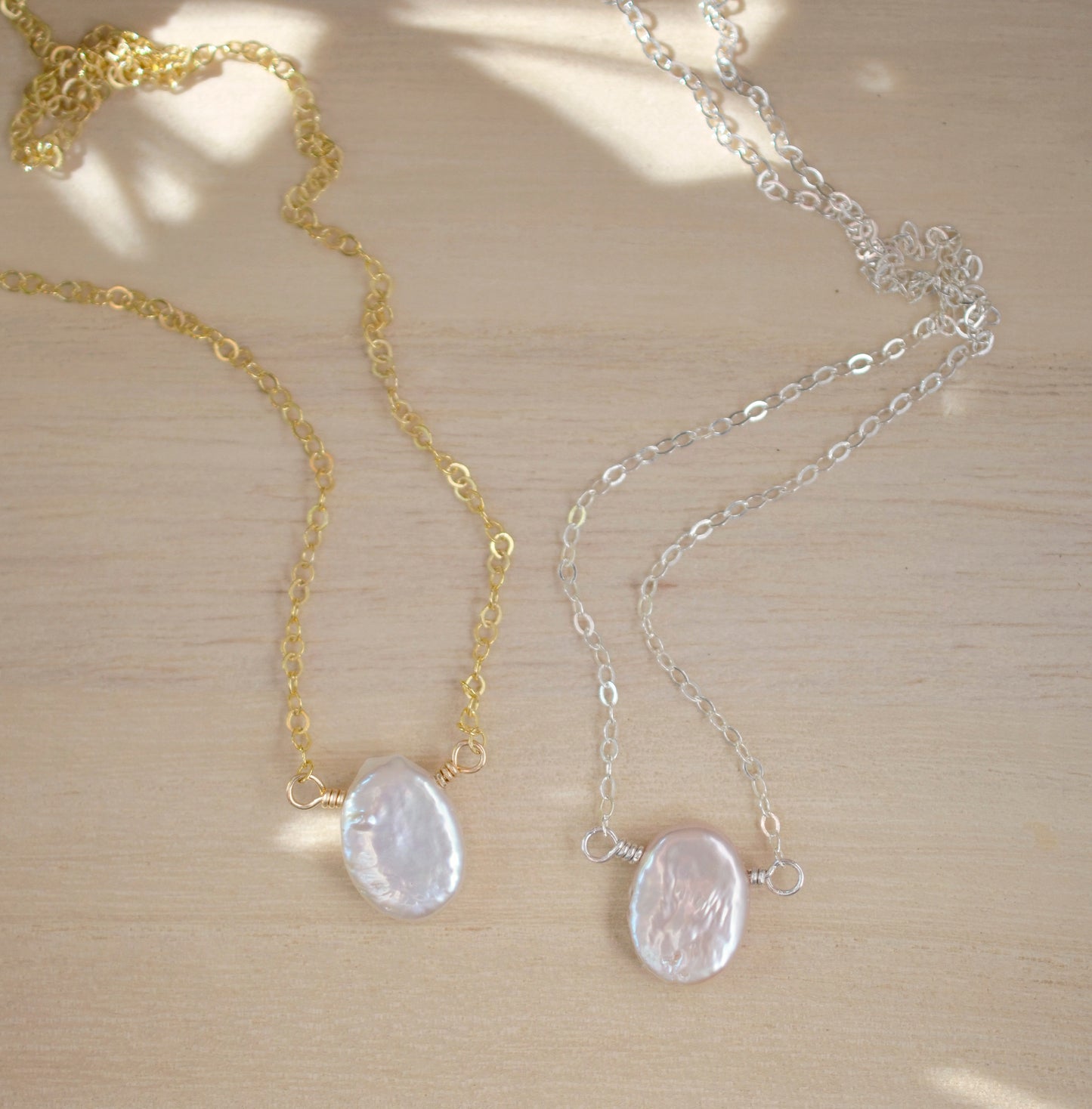 A dainty flat, oval-shaped white freshwater pearl is set within a 14k gold filled or sterling silver chain. Both styles are shown.