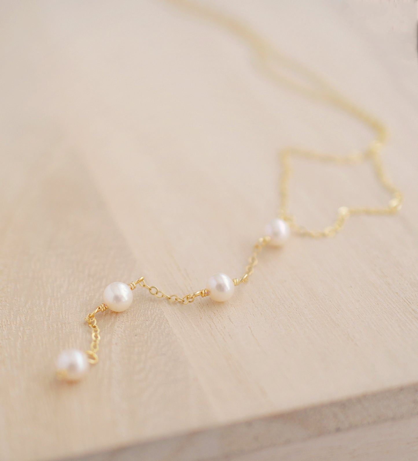 Four semi-round white freshwater pearls are suspended in a Y-style necklace on a 14k gold filled chain. Each pearl is approximately one inch apart. This necklace is also available in sterling silver.
