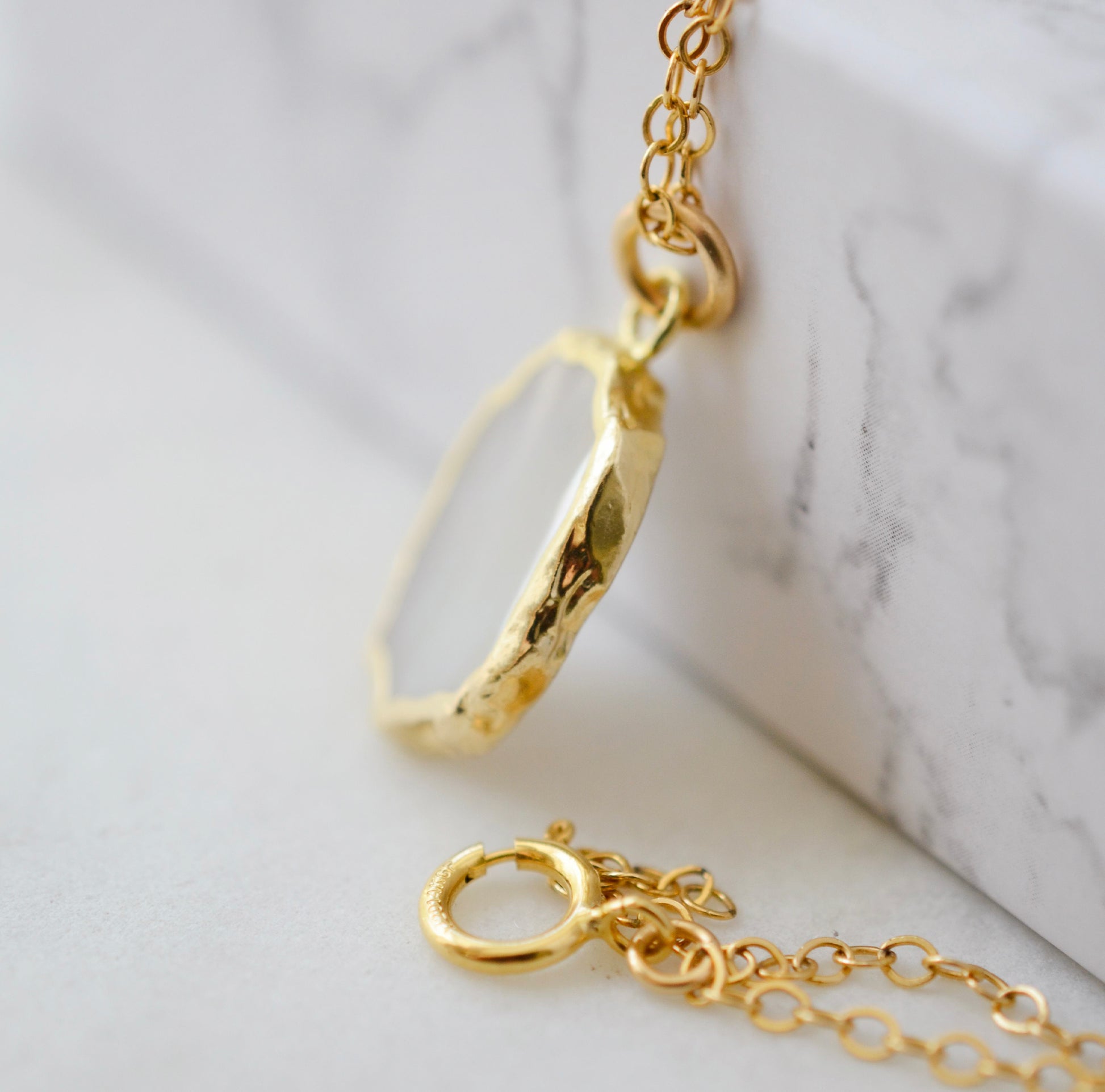 Side view of bezel. A smooth polished natural, white mother of pearl slice has been set in a 24k gold electroplated bezel and suspended from a 14k gold filled chain. The shell shimmers in shades of white, silver, and pink.