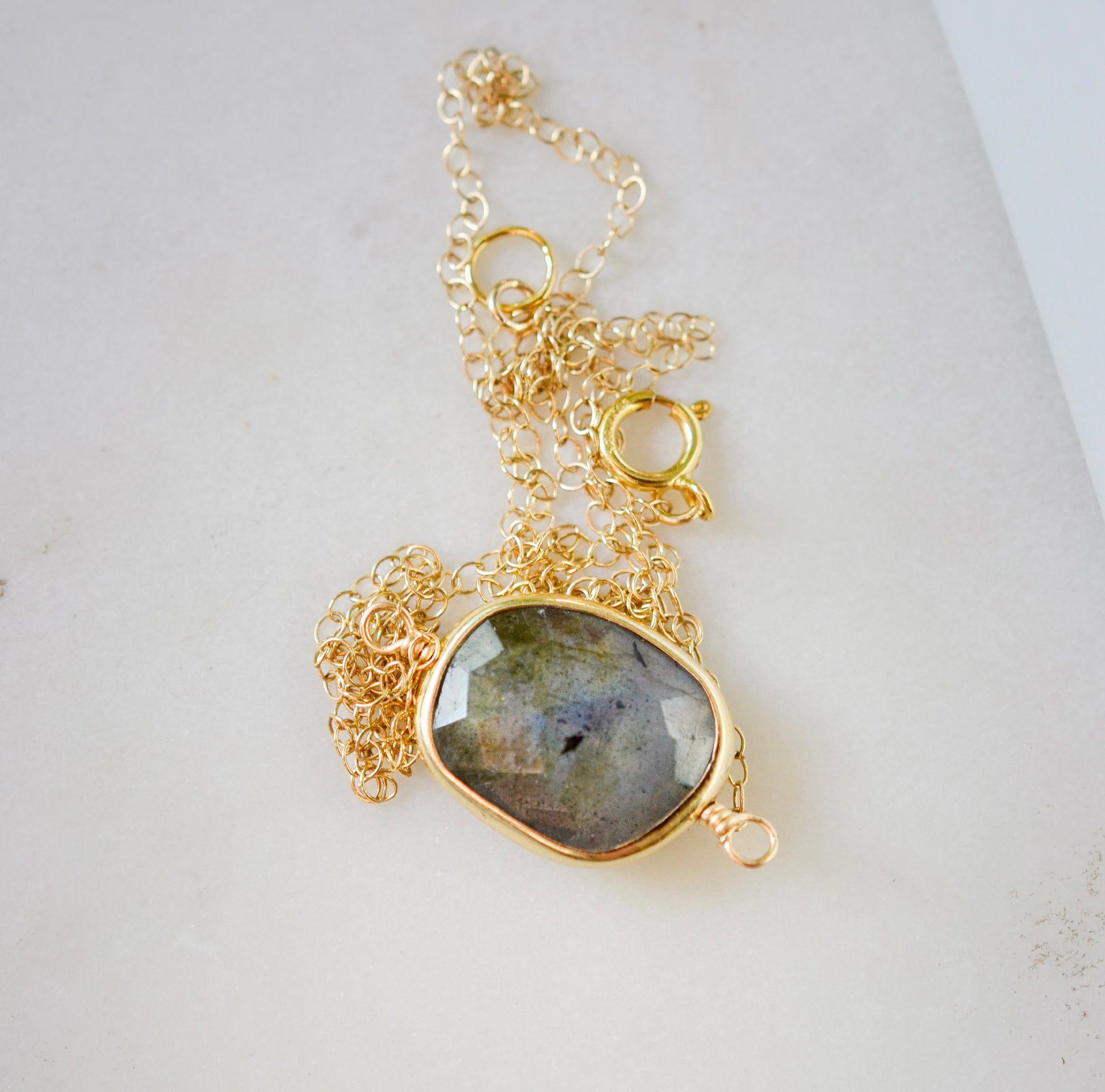 A gold Labradorite necklace. The handmade pendant pendant is bezeled in gold and set on a 14k gold filled chain. This necklace is also available in sterling silver. The stone is oval in shape and flashes blue, green, or yellow.