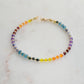 Beaded gemstone bracelet in rainbow colors. Handmade with natural gemstones including: yellow agate, orange carnelian, wine-red garnet, amethyst, tanzanite, topaz, and green emerald. Shown with a gold clasp.