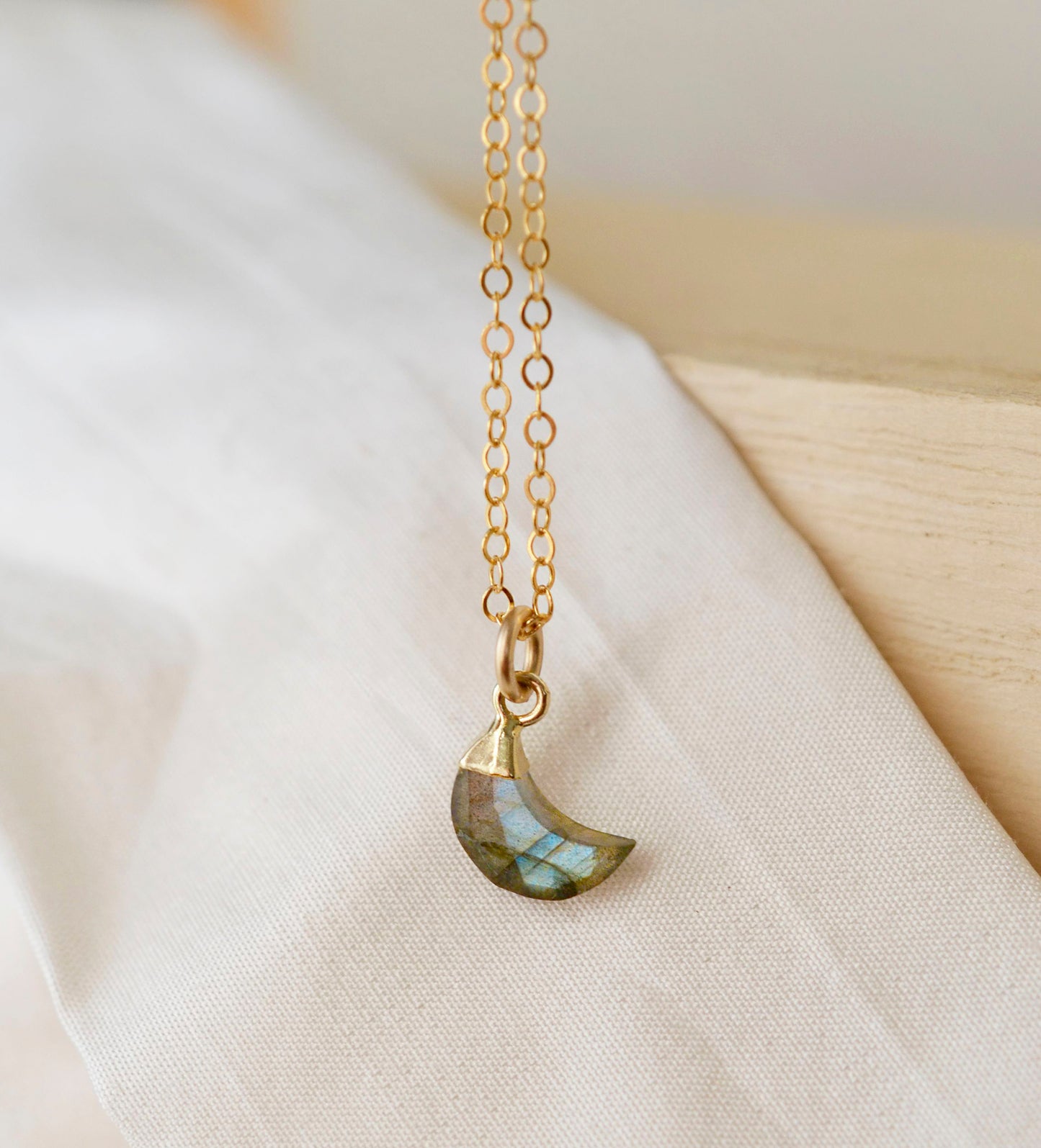 A gold-filled chain necklace with a faceted crescent moon-shaped labradorite gemstone pendant. Handmade in Connecticut.