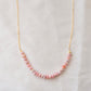 Natural pink Rhodochrosite beaded handmade necklace shown in 14k gold filled. The gemstones vary in shades of pink, peach, white, and gray and are faceted rondelle shape. They span approximately 4 inches across the front of the necklace, then attach to a dainty cable chain. Also available in sterling silver.