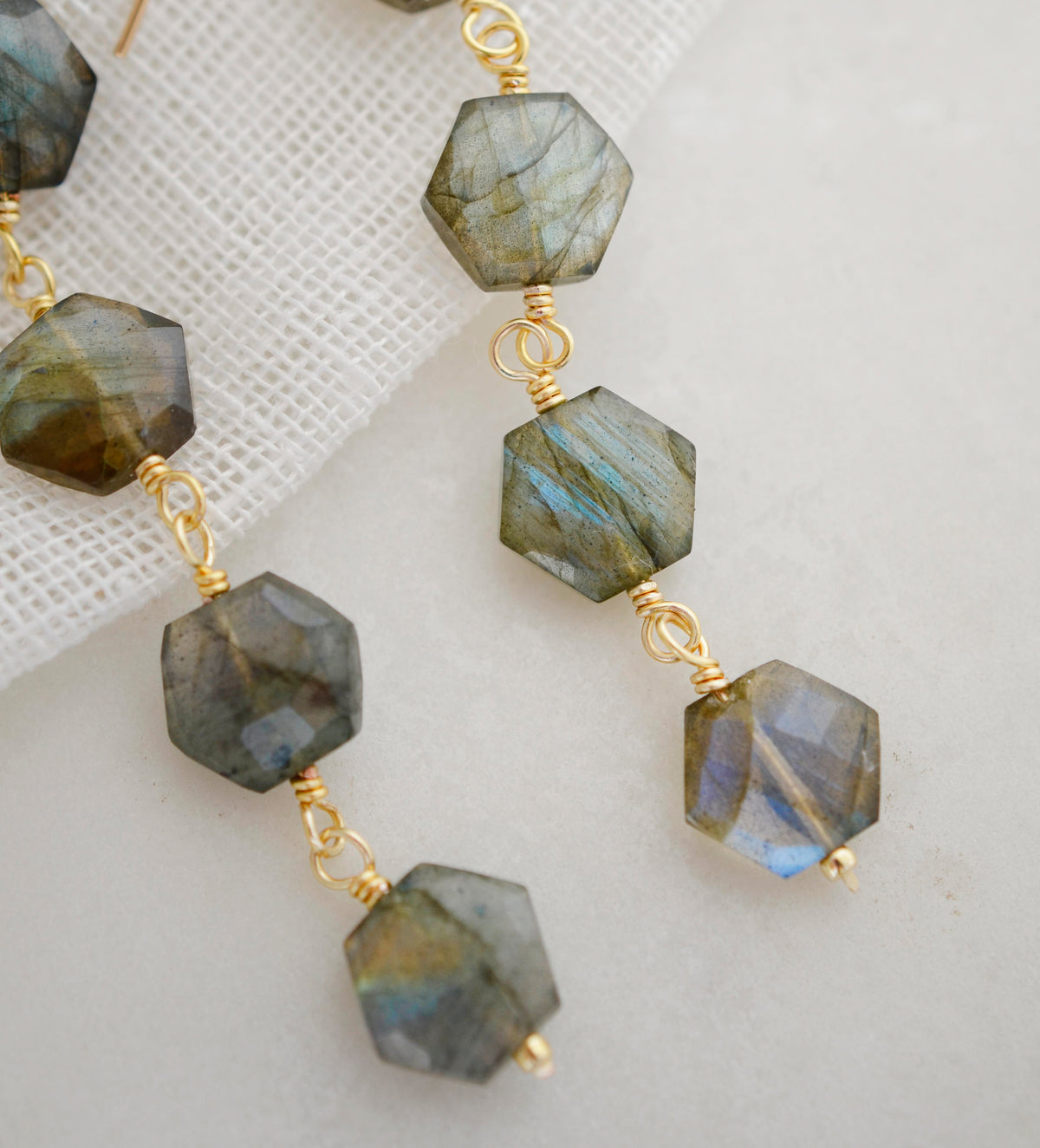 A close up image of long hexagonal shaped labradorite gemstone earrings. These dangles are handmade and available in sterling silver or 14k gold filled. 