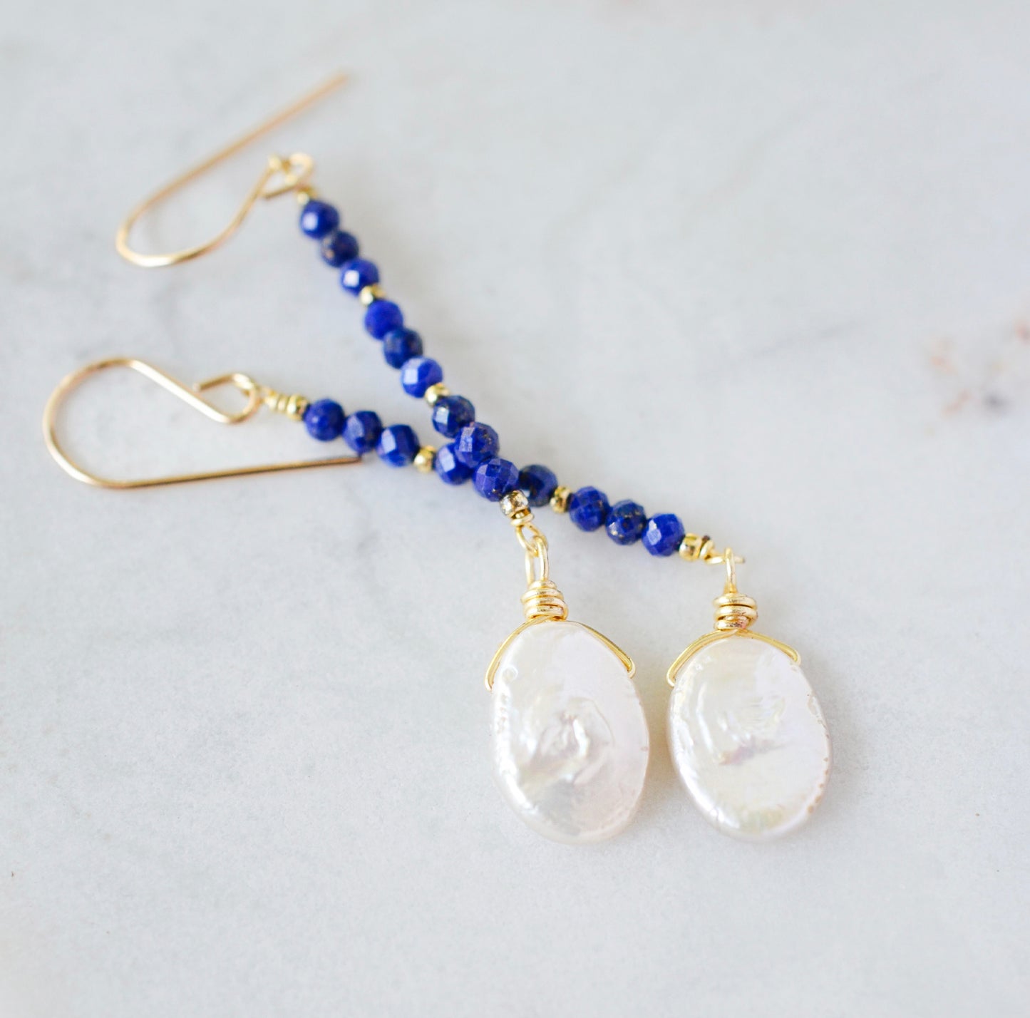 Natural blue lapis lazuli gemstone and white freshwater pearl long dangle earrings. The dangles are long and thin with oval freshwater pearls at the end. They come in 14k gold filled and sterling silver.