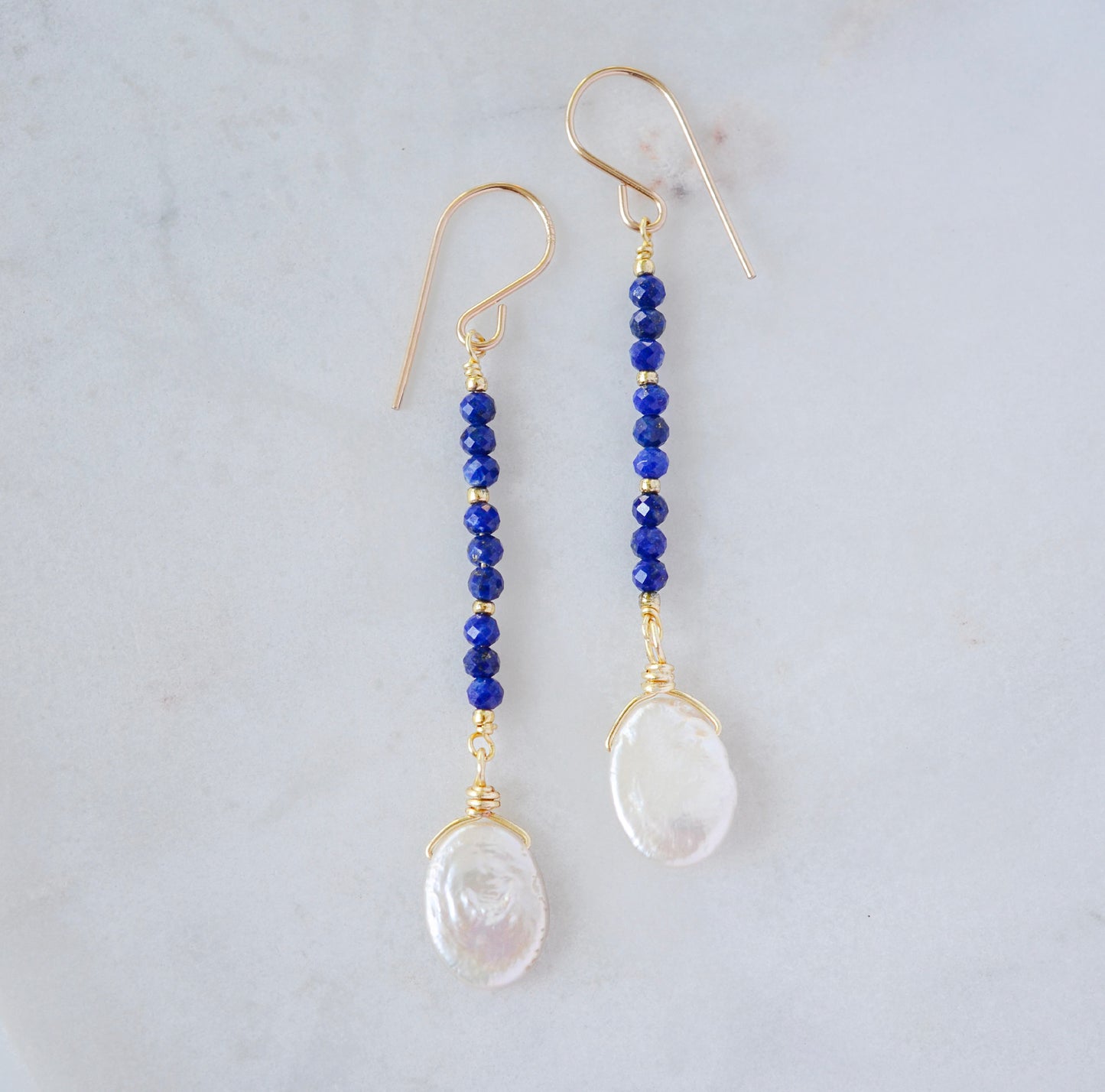 Natural blue lapis lazuli gemstone and white freshwater pearl long dangle earrings. The dangles are long and thin with oval freshwater pearls at the end. They come in 14k gold filled and sterling silver.