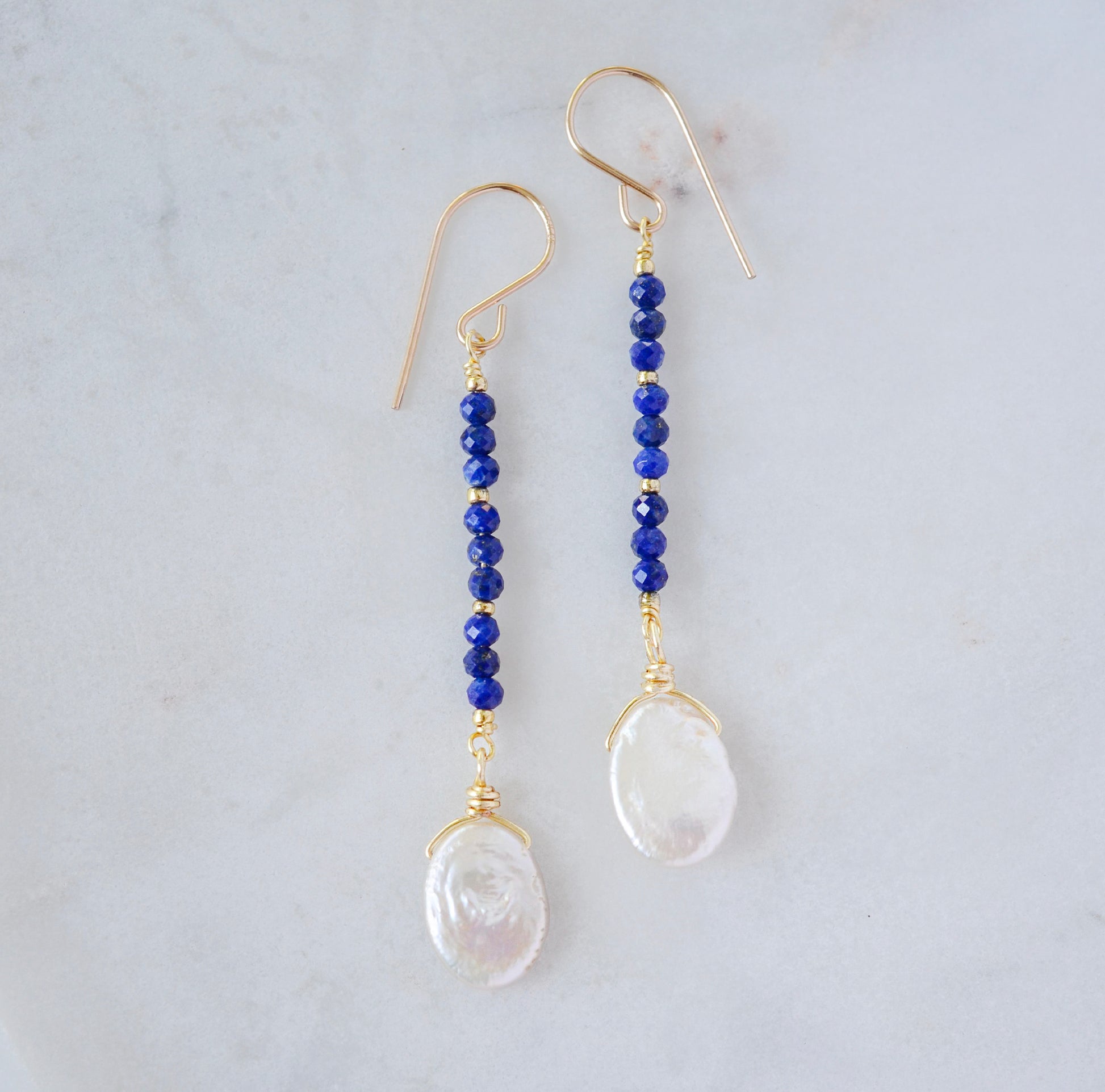 Natural blue lapis lazuli gemstone and white freshwater pearl long dangle earrings. The dangles are long and thin with oval freshwater pearls at the end. They come in 14k gold filled and sterling silver.