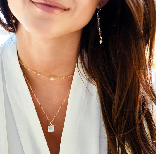 Close-up of a woman wearing layered gold gemstone and pearl necklaces and earrings. All jewelry is handmade in Connecticut USA by Gemnia.