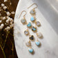 These handmade earrings feature blue and white natural stone hearts bezeled in gold. Each gemstone is a different color and includes: labradorite, larimar, mother of pearl, aquamarine, and rainbow moonstone. Long and light weight they make the perfect romantic gift. They are 3 inches long.