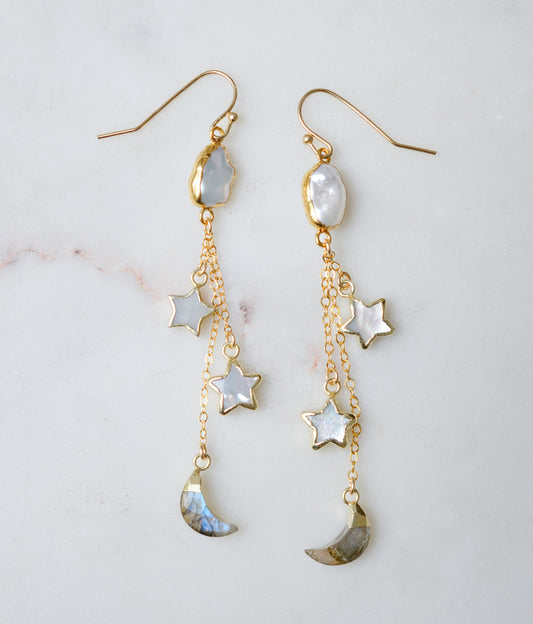 Long gold dangle earrings with star and moon charms on a light background. The stones are freshwater pearl, labradorite, and mother of pearl.