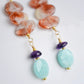 Three sunstone gemstone dangle atop amethyst and amazonite stones. The earring are shown in gold. Close up of amethyst and amazonite.