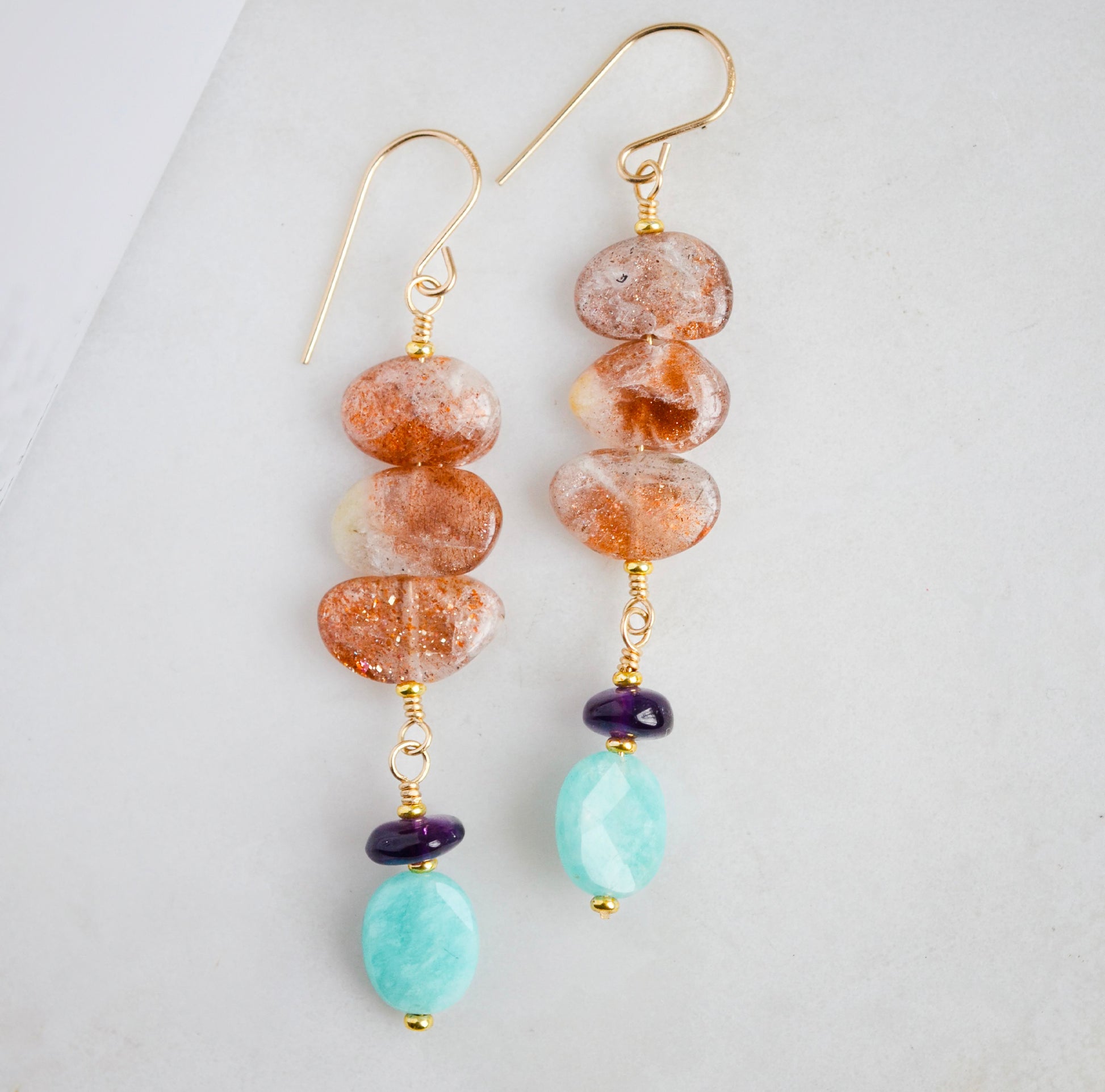 Three sunstone gemstone dangle atop amethyst and amazonite stones. The earring are shown in gold. 