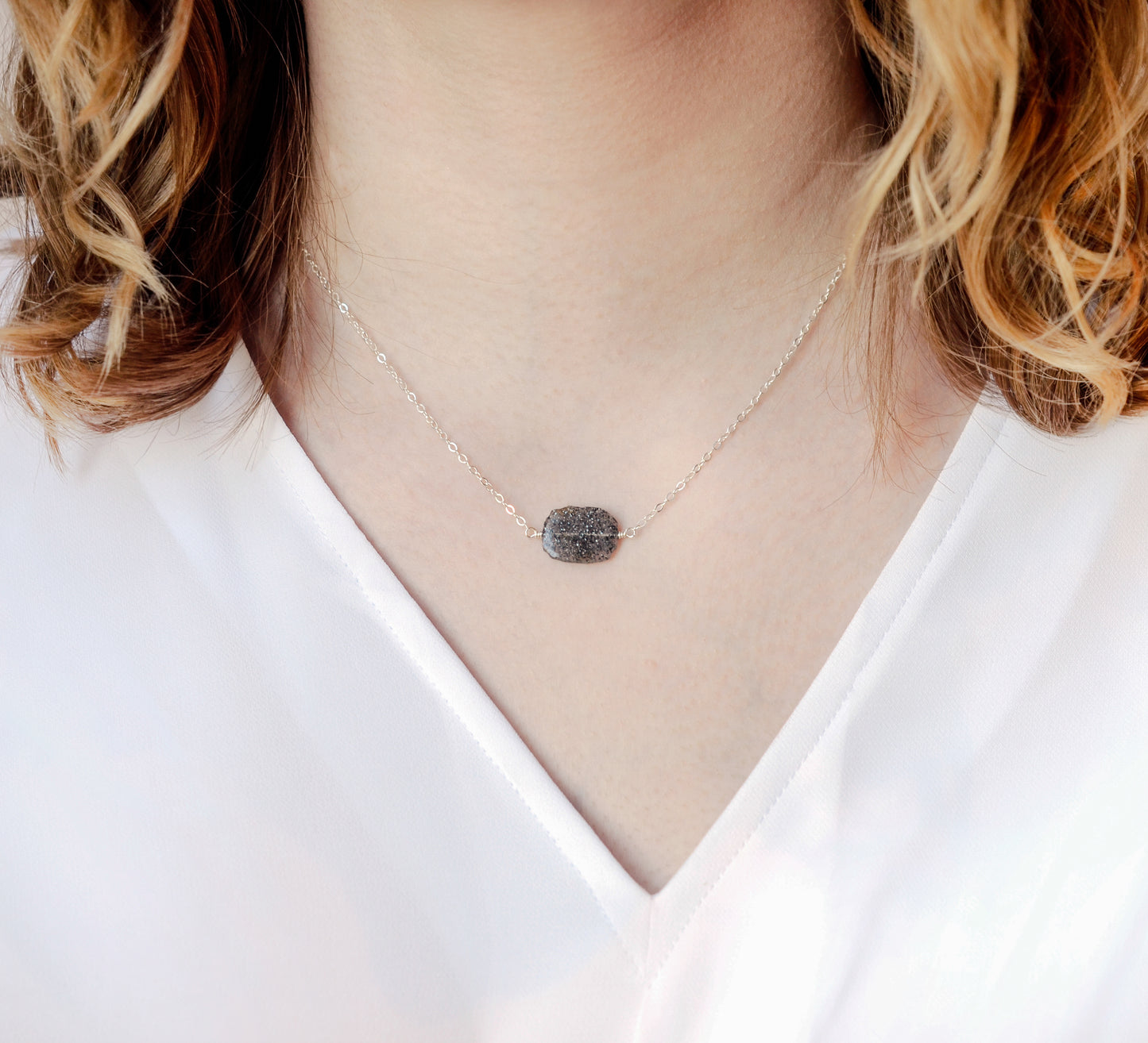 Genuine raw black sunstone gemstone set on a sterling silver chain. The shape of the stone is irregular. Modeled image.