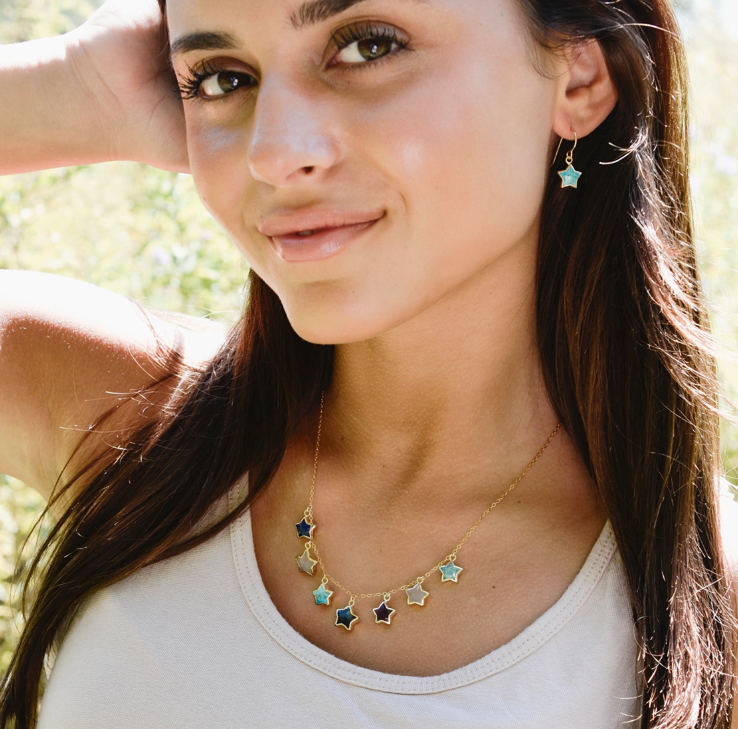 Woman wearing a gold necklace with star-shaped pendants and turquoise celestial earrings. Handmade jewelry by Gemnia in Connecticut.